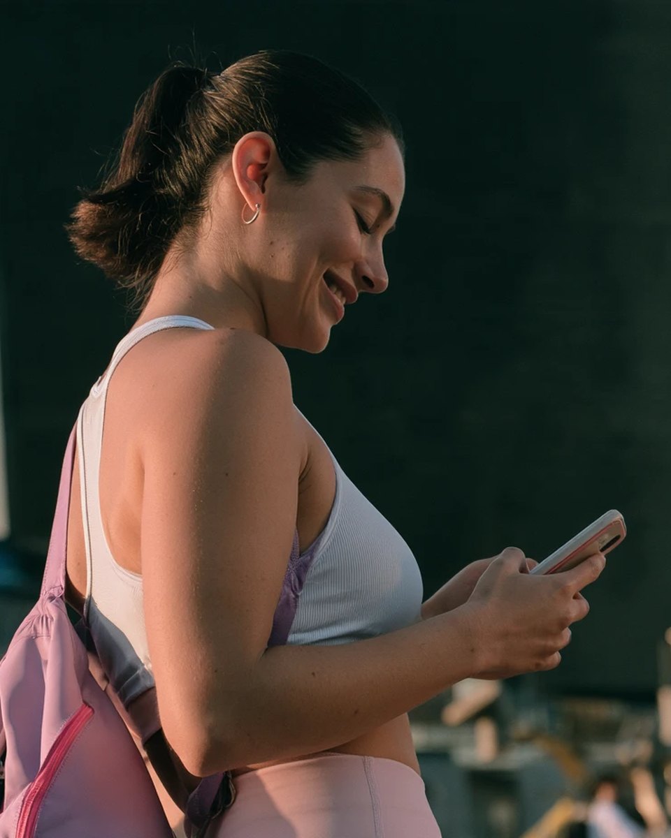 A smiling woman with a gym bag filling out a form on her phone